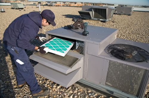 worker replacing a blue air filter in an outside HVAC unit